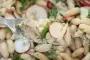 Warm white bean salad with radish slices and sardine fillets.